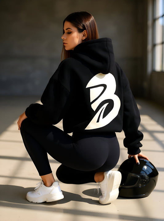 Model wearing the Brontailia Classic Hoodie in black with large white B logo on the back